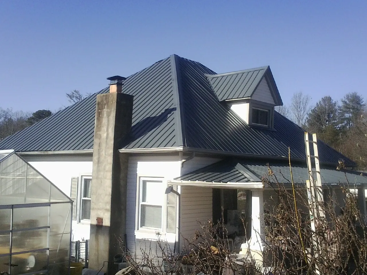 Dark blue standing seam metal roof on a white farmhouse with dormer — Slate & Tile Roof Repair by Roofing Brothers in Hanceville