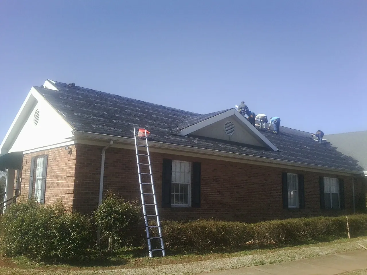 Crew tearing shingles off a brick ranch roof with a ladder set — Metal Roof Repair work by our crew in Hanceville