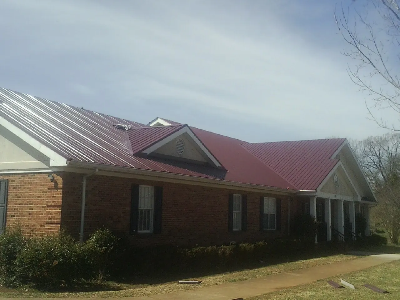 Red metal roof with gabled entries on a long brick building, from a Hail Damage Roof Repair job in Hanceville