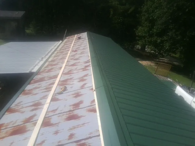 Old rusted panels beside newly installed green metal roofing — Wind Damage Roof Repair by Roofing Brothers in Hanceville