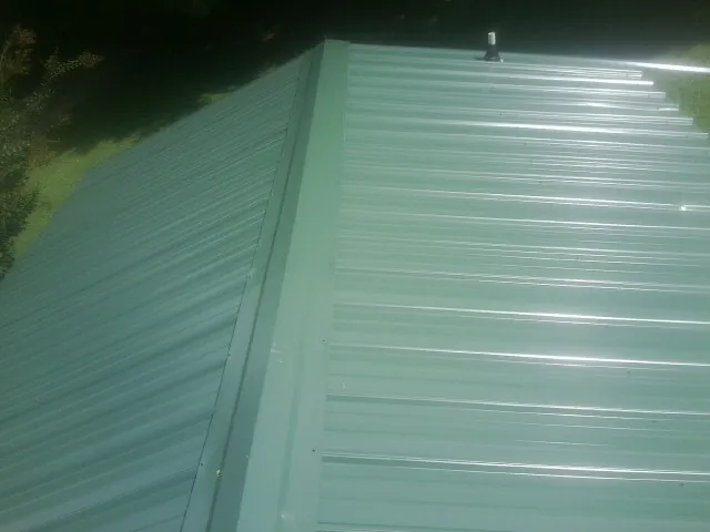 New green metal panels meeting at the ridge of a roof — Flat Roof Repair work by our crew in Hanceville