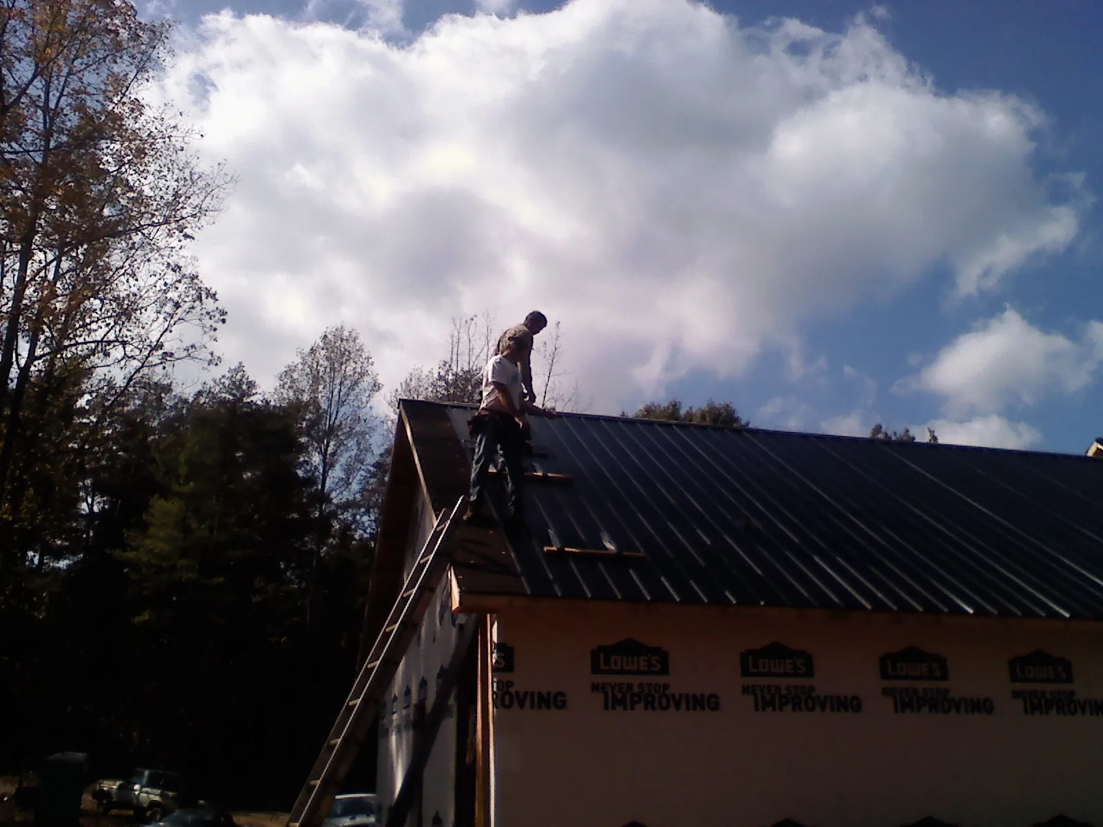Roofer fastening dark metal panels high against a cloudy sky, from a Roof Inspection job in Hanceville