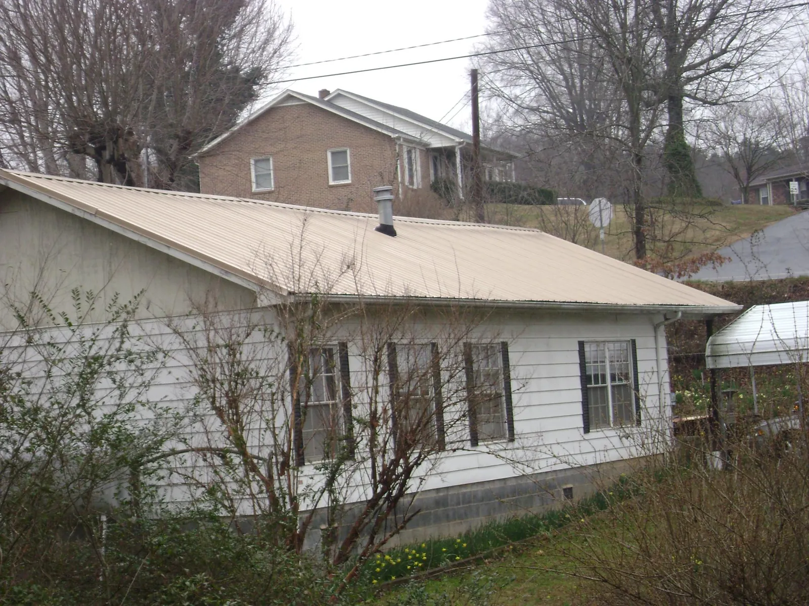 Tan metal roof on a white sided house set into a hillside — Commercial Roofing by Roofing Brothers in Hanceville