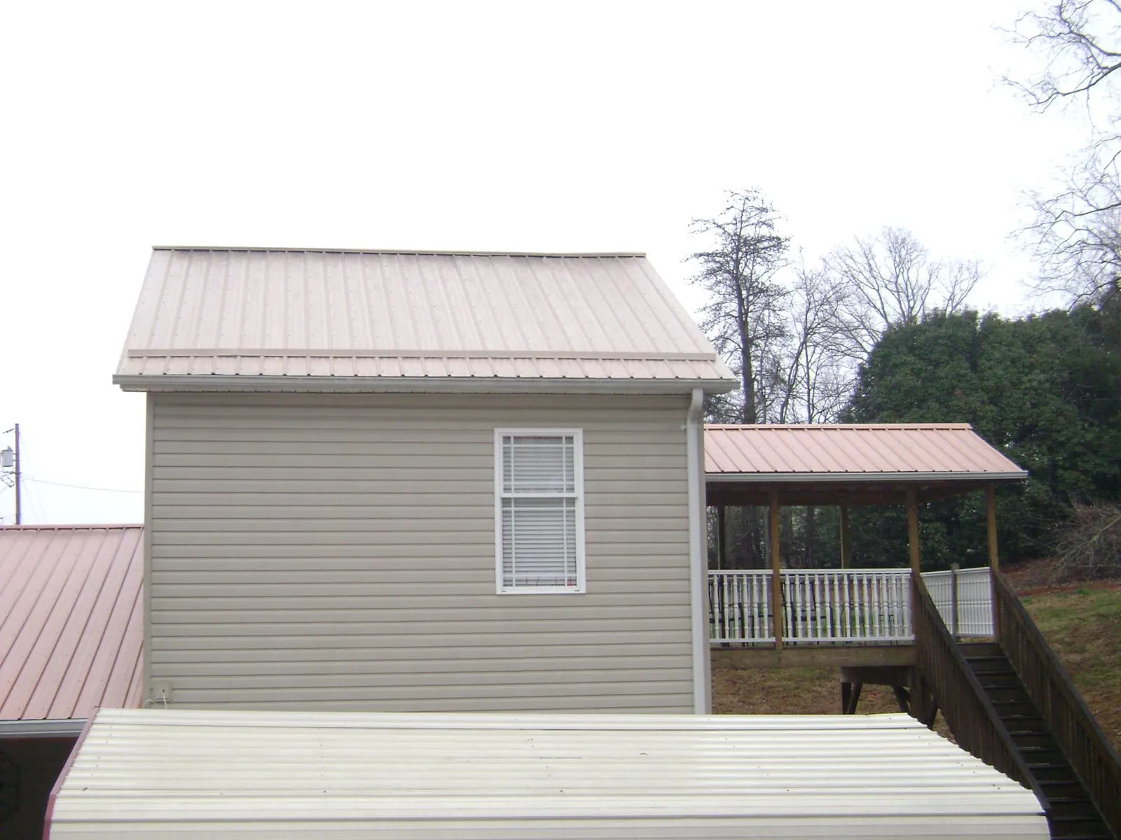 Tan metal roofs on a two story addition and attached porch, from a Roof Replacement job in Hanceville